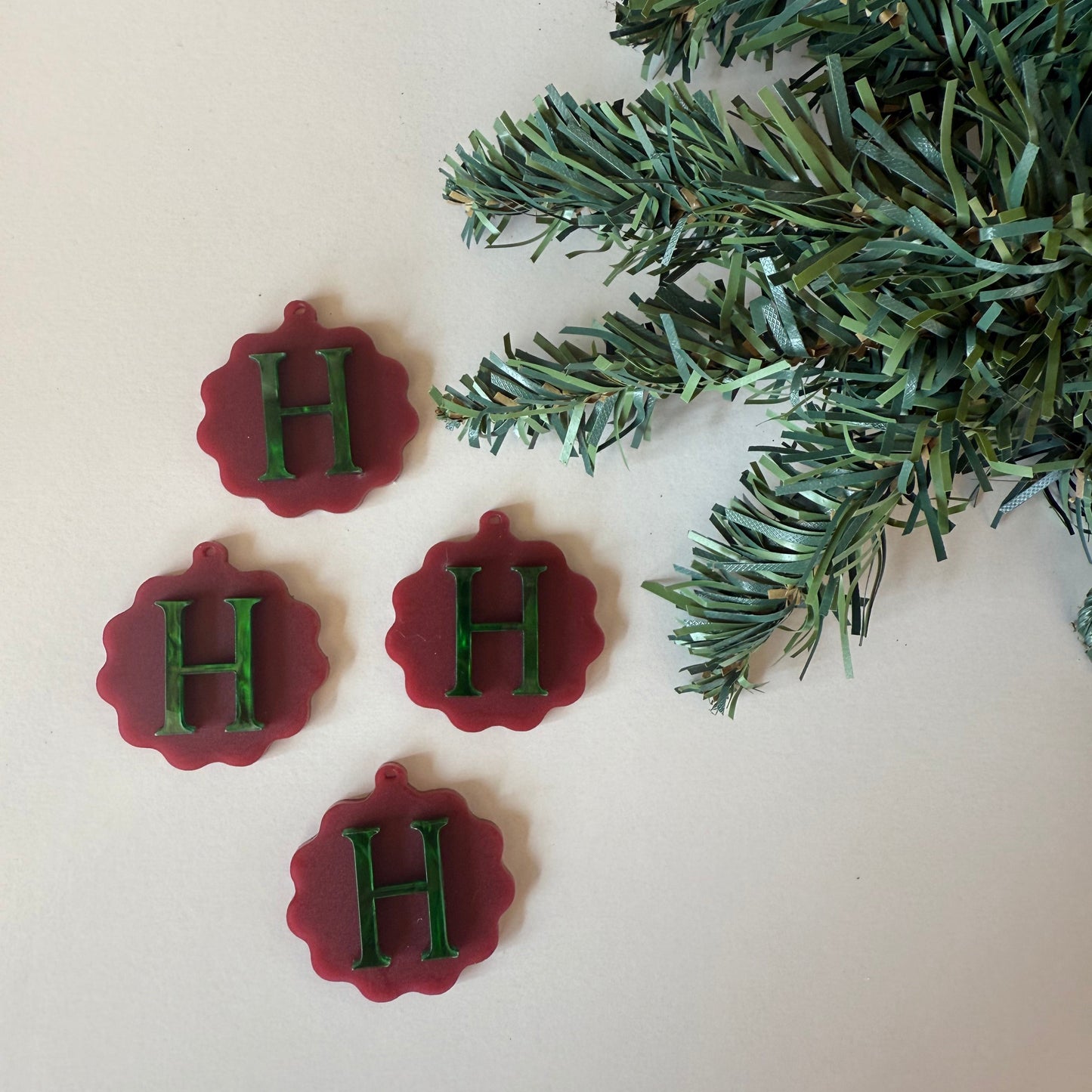 Red and green decorative items with 'H' on a white background with Christmas tree branches.